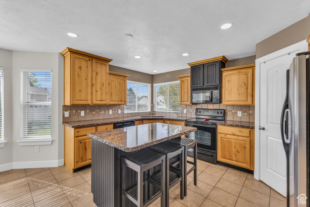 Kitchen featuring sink, tasteful backsplash, a kitchen island, black appliances, and dark stone countertops