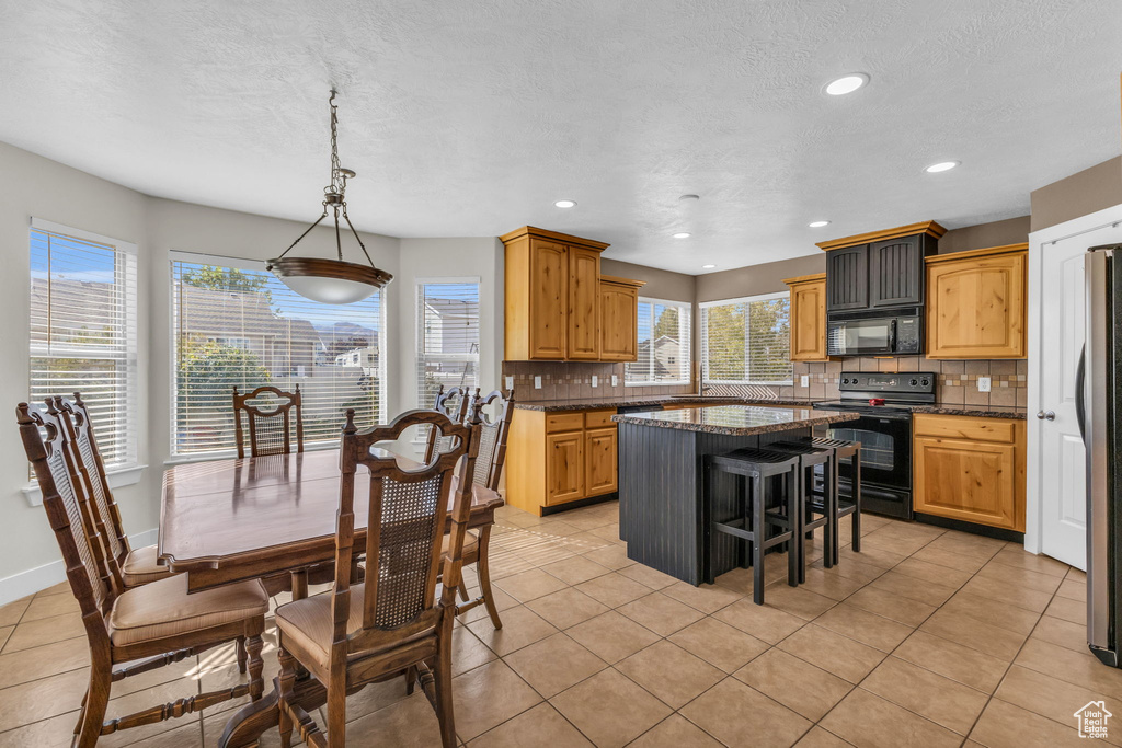 Kitchen with a kitchen island, black appliances, tasteful backsplash, pendant lighting, and light tile patterned floors