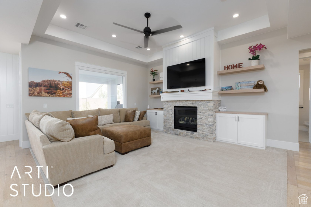 Living room featuring light hardwood / wood-style floors, ceiling fan, a tray ceiling, and a stone fireplace