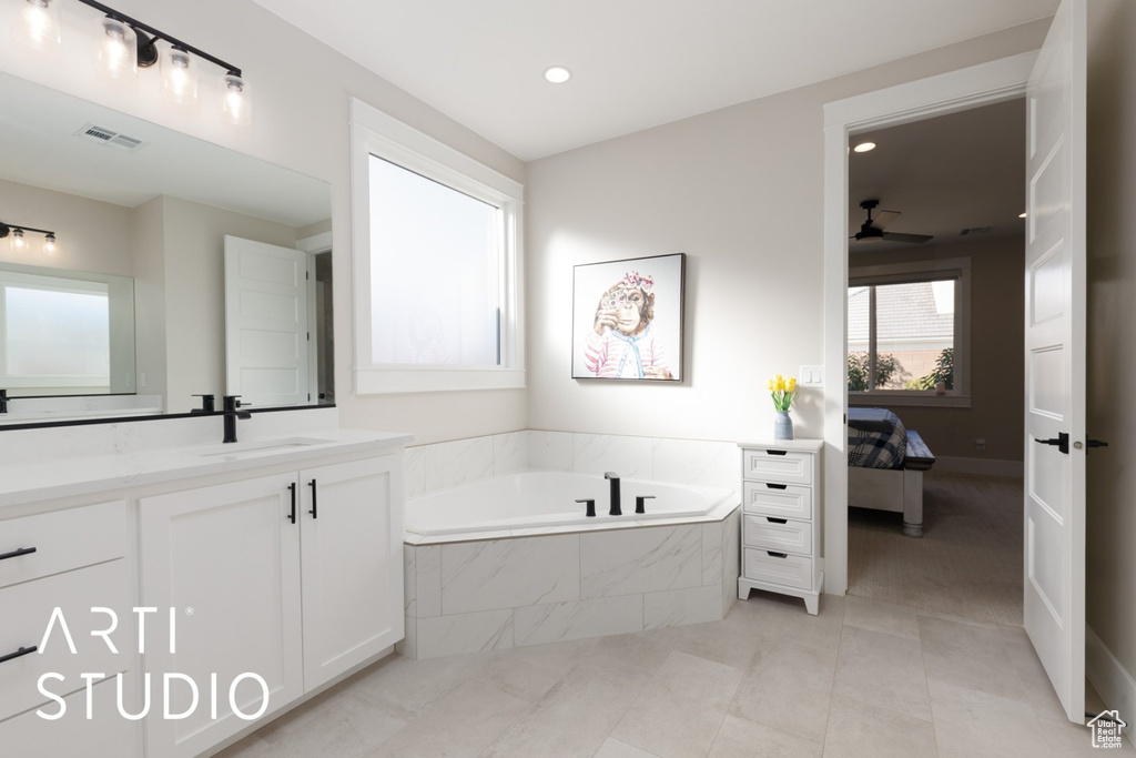 Bathroom with tiled tub, vanity, tile patterned flooring, and ceiling fan