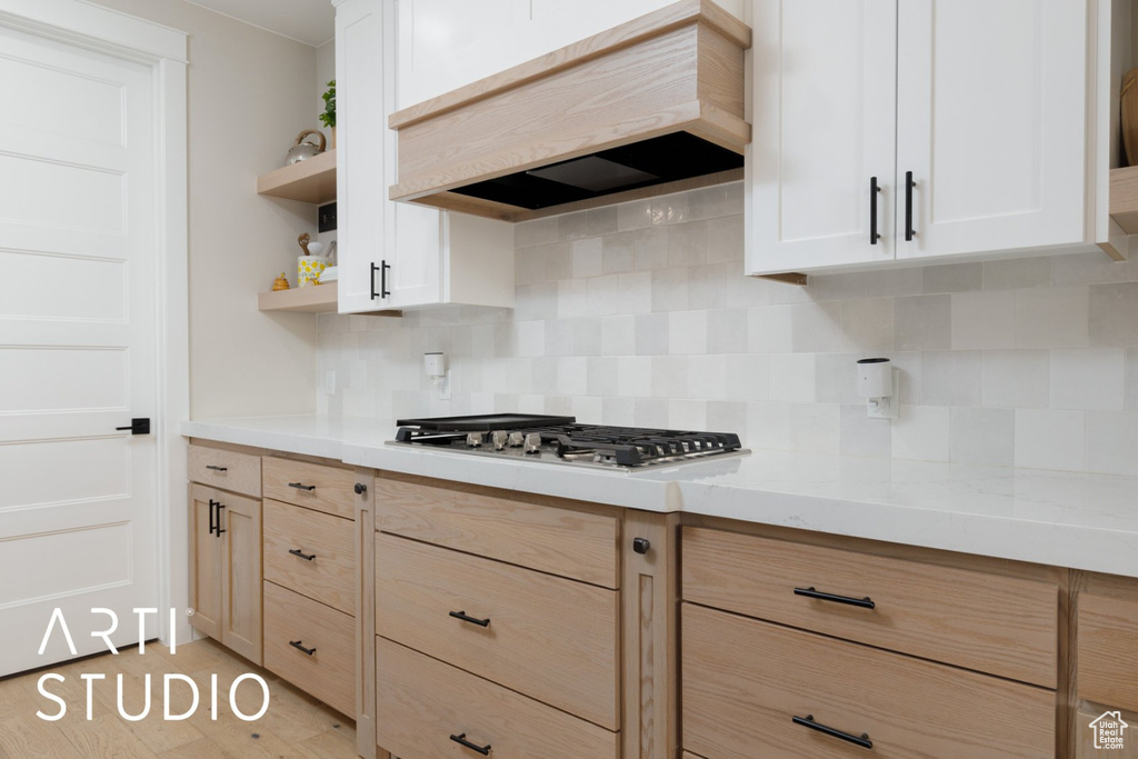 Kitchen featuring light stone counters, decorative backsplash, stainless steel gas cooktop, white cabinetry, and custom exhaust hood