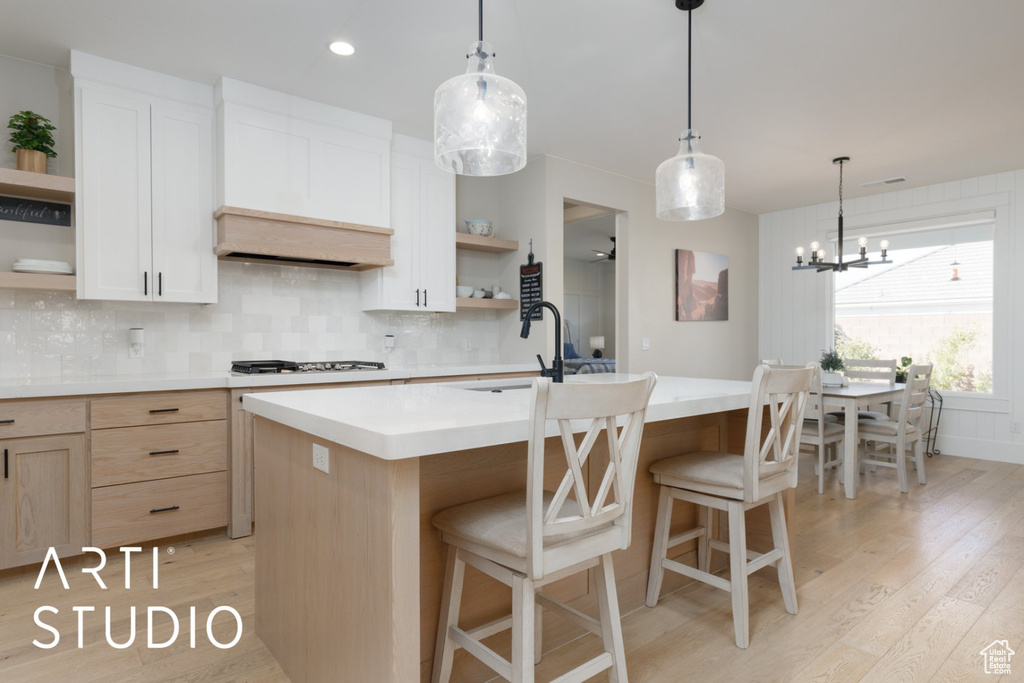 Kitchen featuring a kitchen island with sink, an inviting chandelier, tasteful backsplash, light hardwood / wood-style flooring, and white cabinets