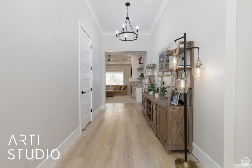 Corridor with ornamental molding, a notable chandelier, and light hardwood / wood-style floors