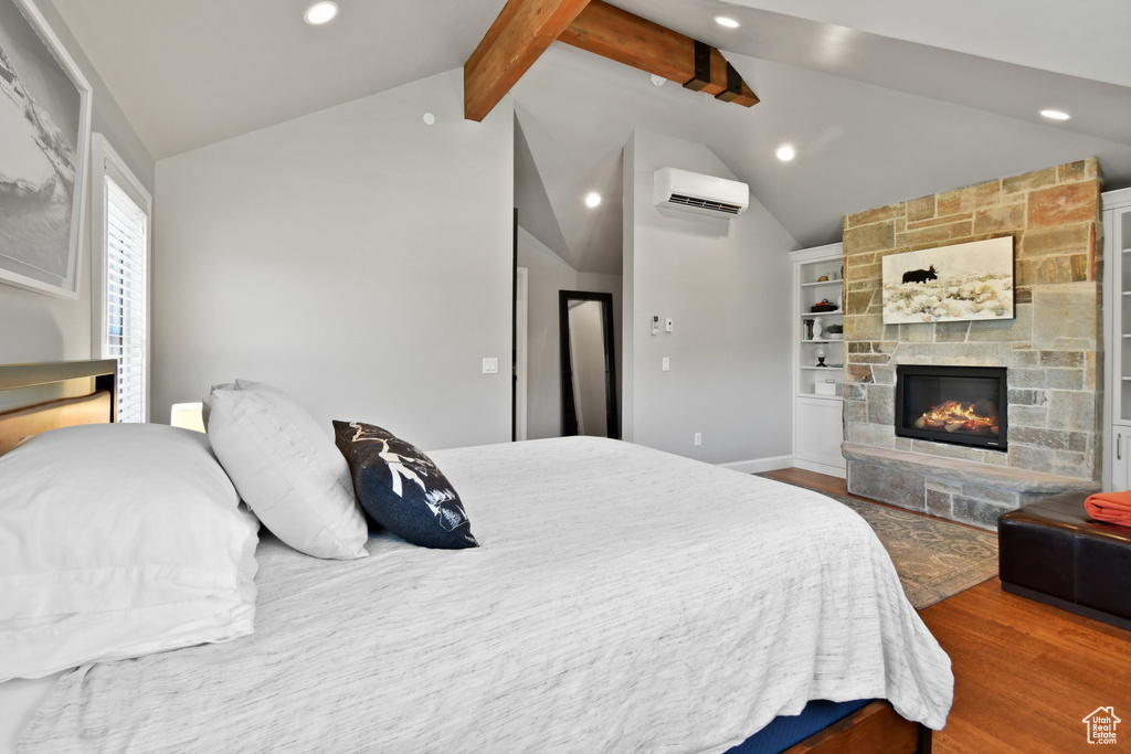 Bedroom featuring a stone fireplace, lofted ceiling with beams, dark wood-type flooring, and a wall mounted AC