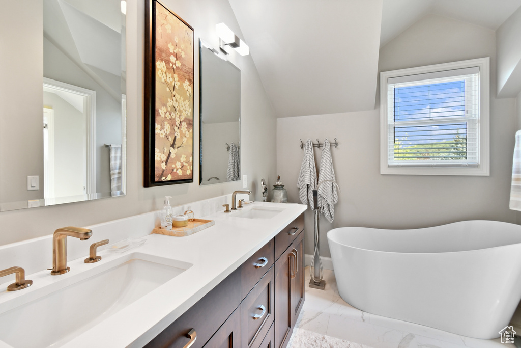 Bathroom featuring a bathtub, vaulted ceiling, and vanity