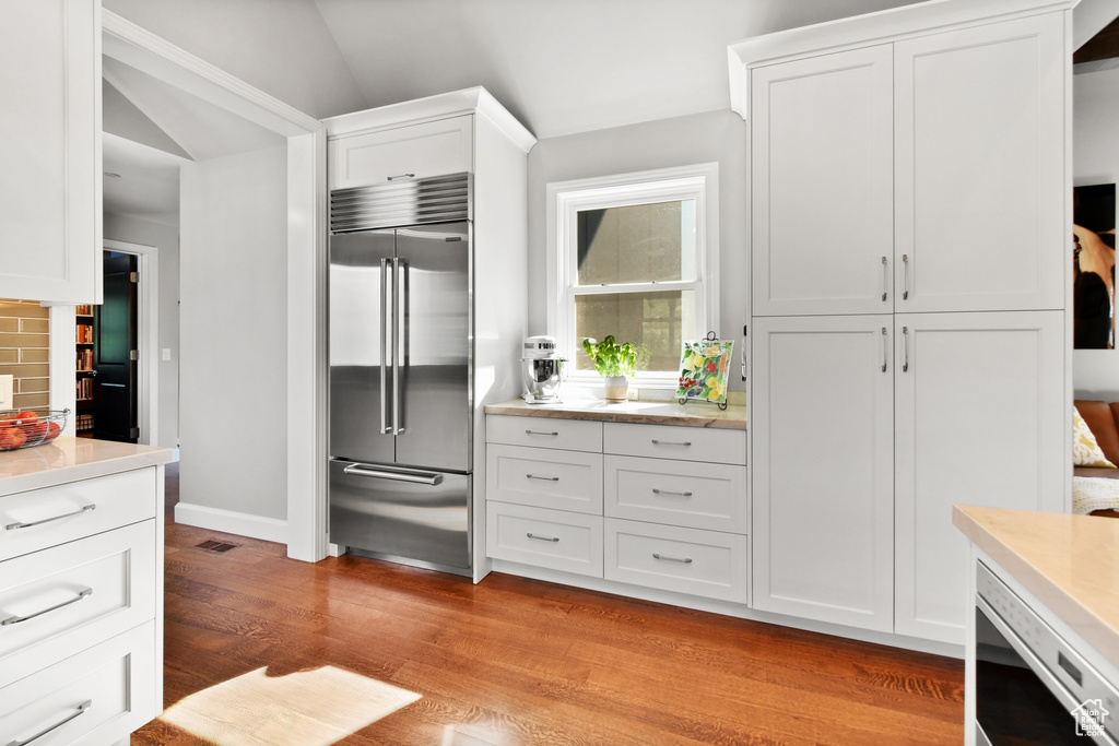 Kitchen featuring lofted ceiling, stainless steel appliances, white cabinetry, light hardwood / wood-style flooring, and backsplash