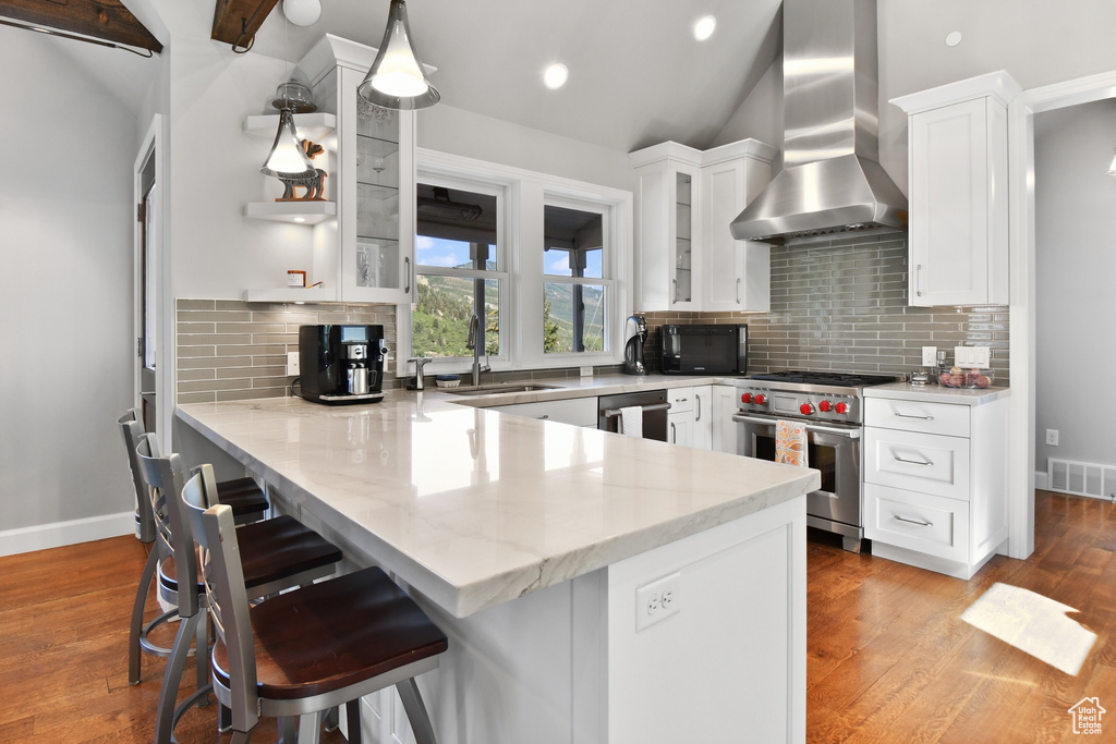 Kitchen featuring stainless steel appliances, wall chimney exhaust hood, kitchen peninsula, a breakfast bar area, and white cabinetry