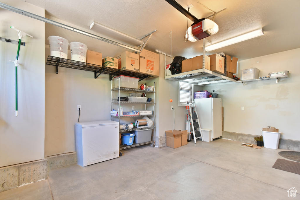 Garage featuring a garage door opener, fridge, and white refrigerator