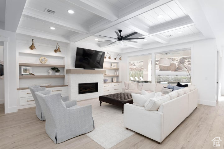 Living room with built in features, light hardwood / wood-style floors, ceiling fan, beam ceiling, and a stone fireplace