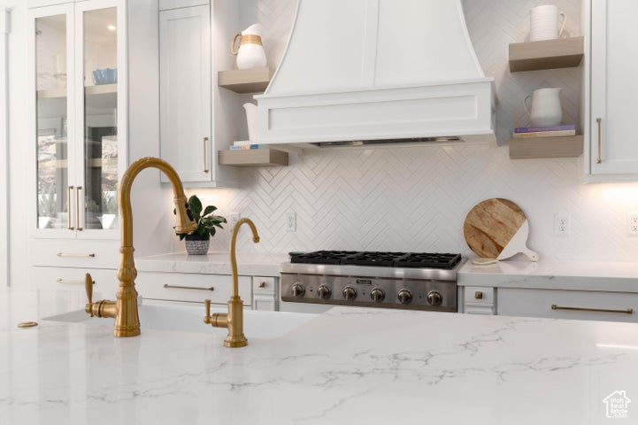 Kitchen with white cabinets, tasteful backsplash, stainless steel appliances, custom range hood, and light stone countertops