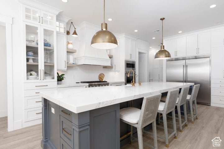 Kitchen featuring pendant lighting, built in appliances, white cabinetry, and a spacious island