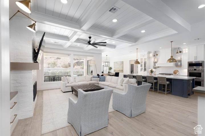 Living room with ceiling fan, a fireplace, beam ceiling, and light hardwood / wood-style floors