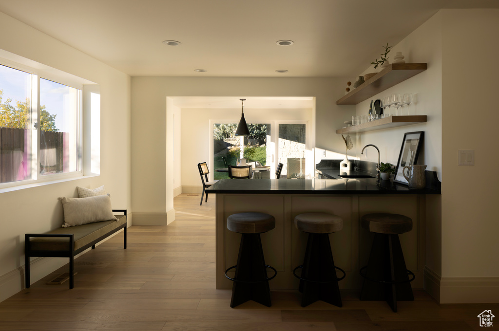 Kitchen with light hardwood / wood-style floors, kitchen peninsula, sink, a breakfast bar, and decorative light fixtures