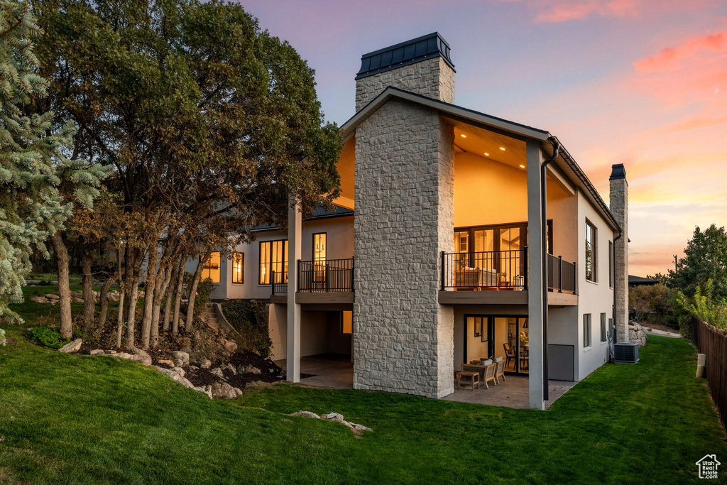 Back house at dusk featuring a lawn, a balcony, and a patio area