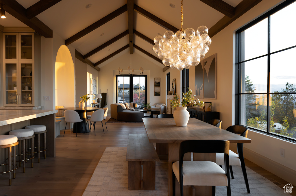 Dining space with hardwood / wood-style flooring, beamed ceiling, an inviting chandelier, and high vaulted ceiling