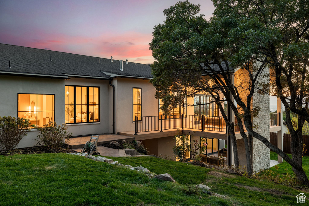 Back house at dusk with a wooden deck and a lawn