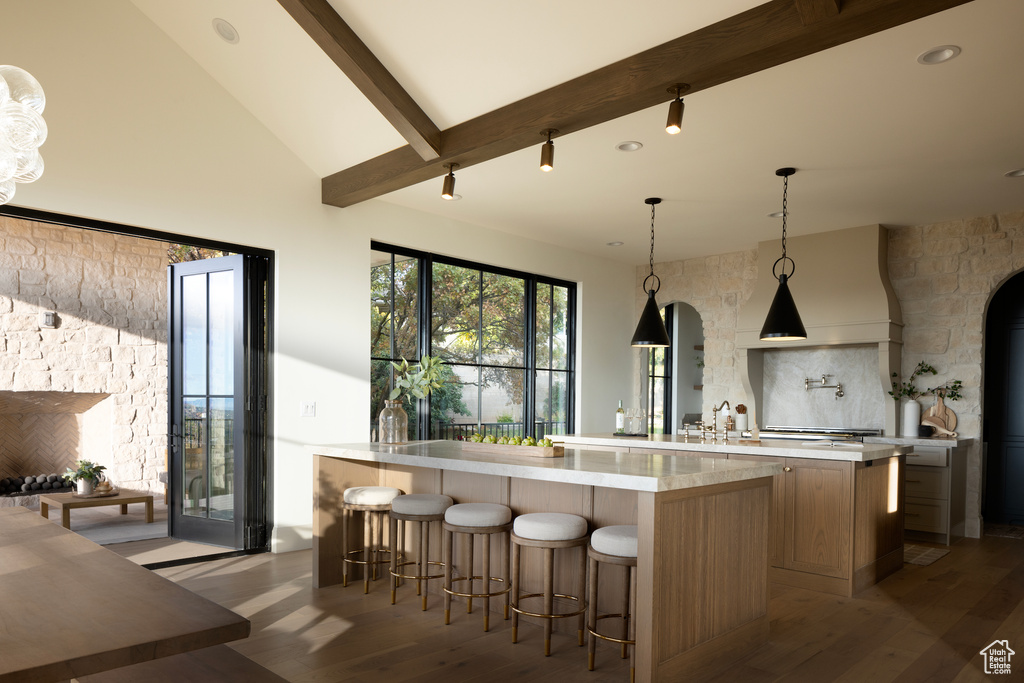 Kitchen featuring hardwood / wood-style flooring, a breakfast bar area, backsplash, hanging light fixtures, and a kitchen island with sink