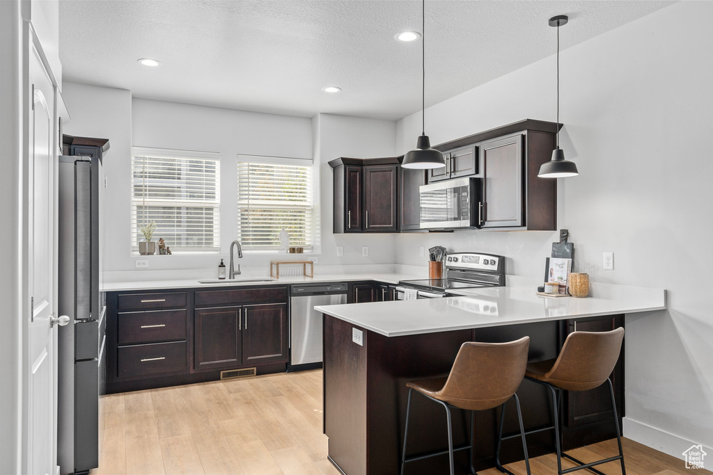 Kitchen with stainless steel appliances, sink, kitchen peninsula, hanging light fixtures, and a breakfast bar area