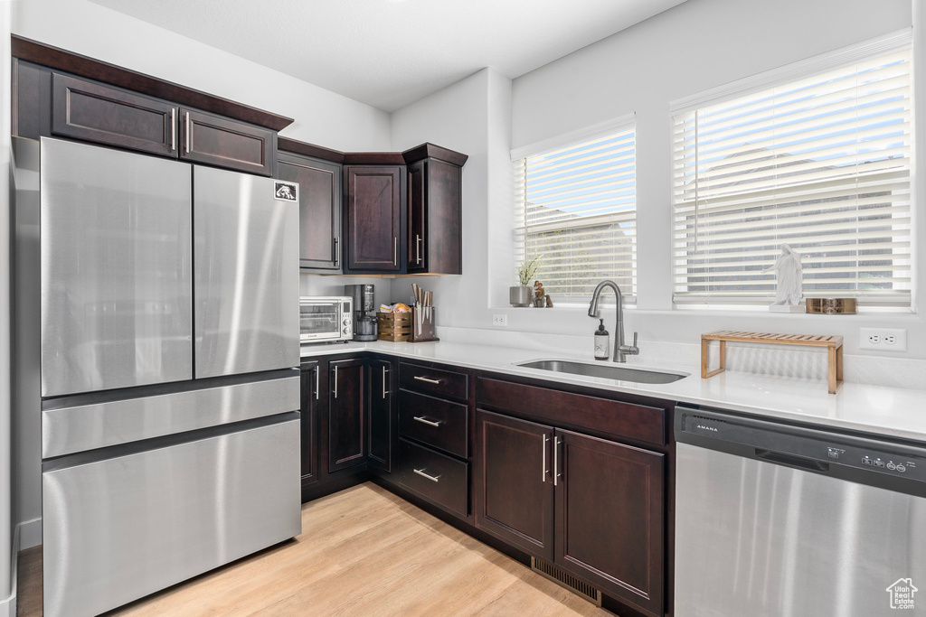 Kitchen featuring dark brown cabinetry, light hardwood / wood-style floors, appliances with stainless steel finishes, and sink