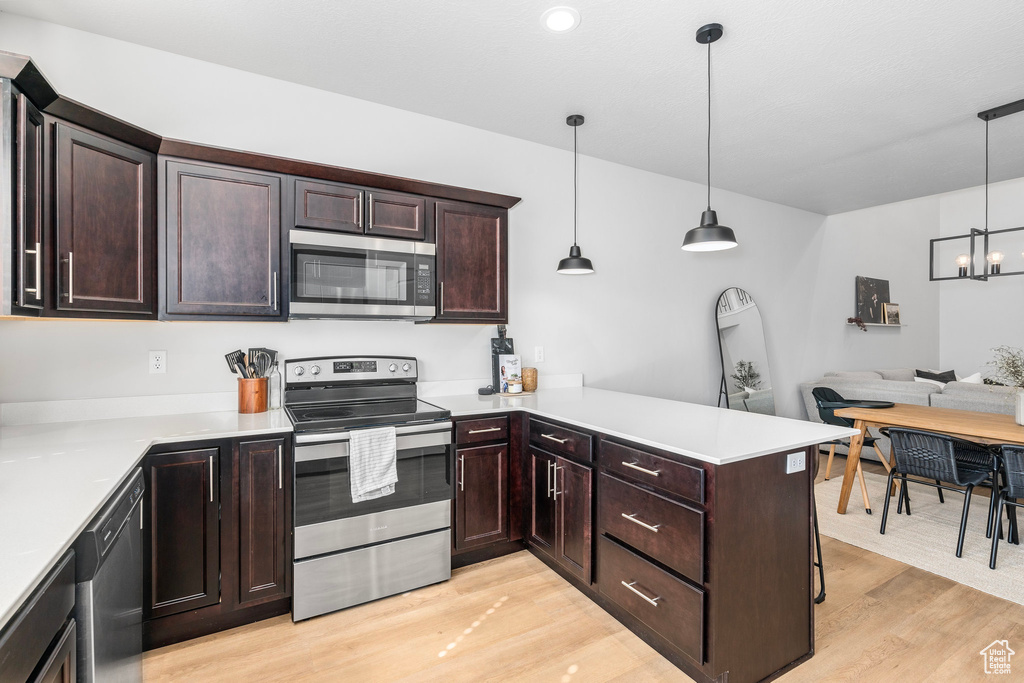 Kitchen with kitchen peninsula, a notable chandelier, hanging light fixtures, light hardwood / wood-style flooring, and appliances with stainless steel finishes