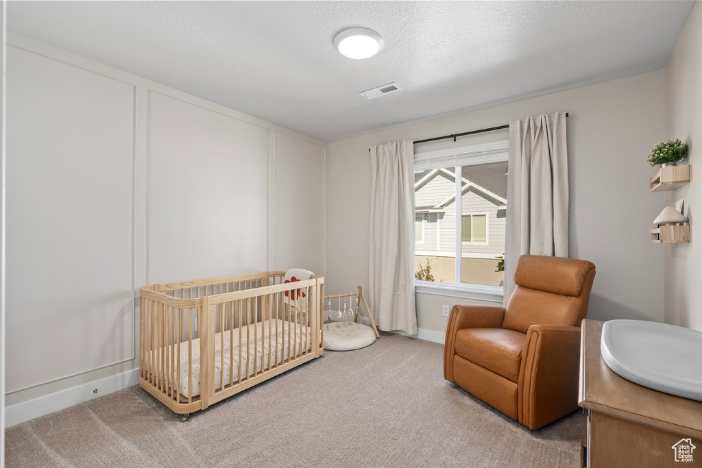 Carpeted bedroom featuring a nursery area and a textured ceiling