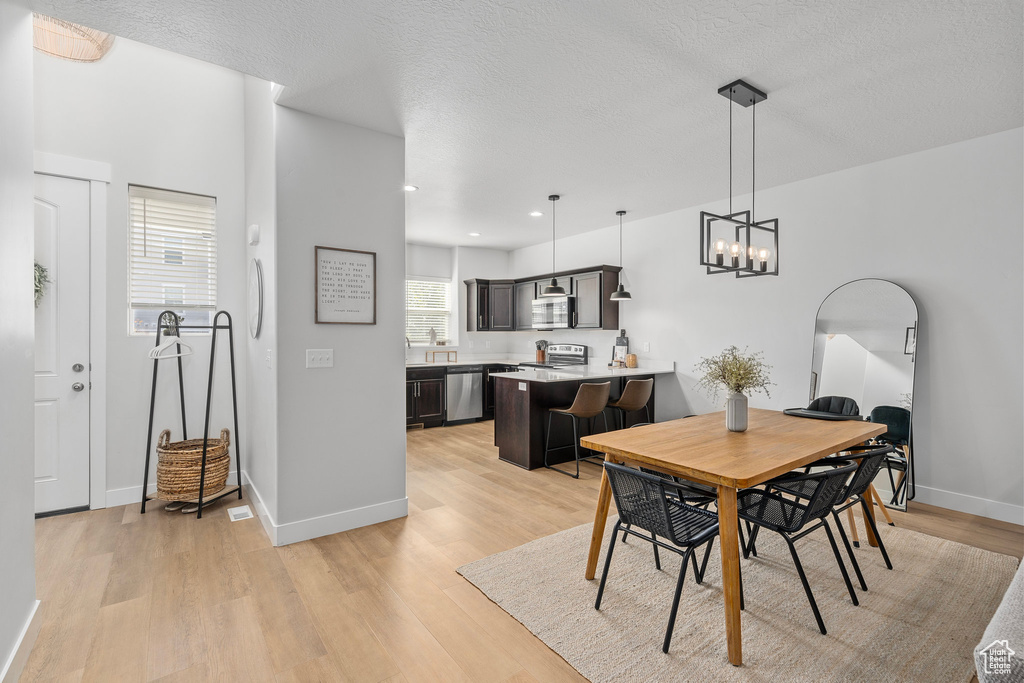 Dining room with a textured ceiling, a chandelier, light hardwood / wood-style floors, and a healthy amount of sunlight