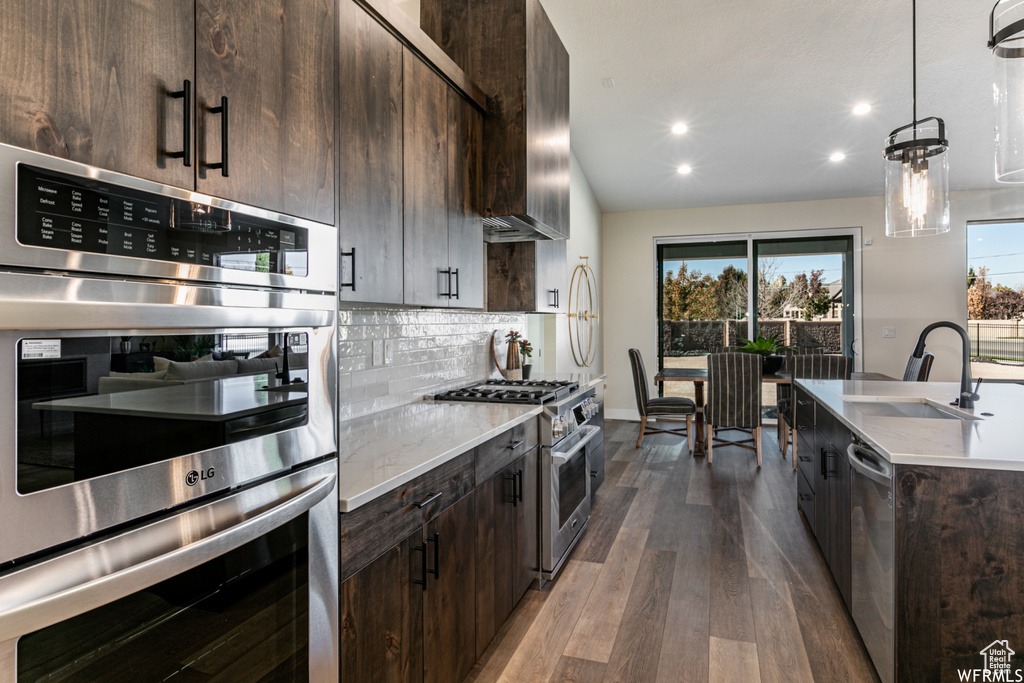 Kitchen with appliances with stainless steel finishes, dark brown cabinetry, decorative light fixtures, and dark hardwood / wood-style flooring