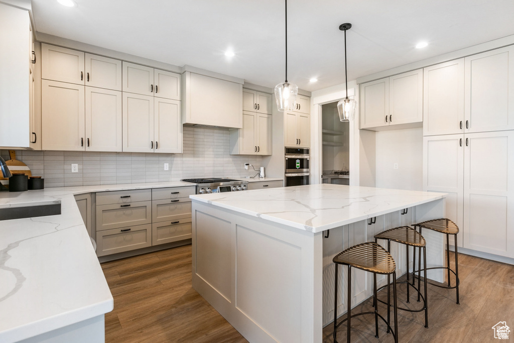 Kitchen with dark wood-type flooring, light stone counters, decorative backsplash, and a center island