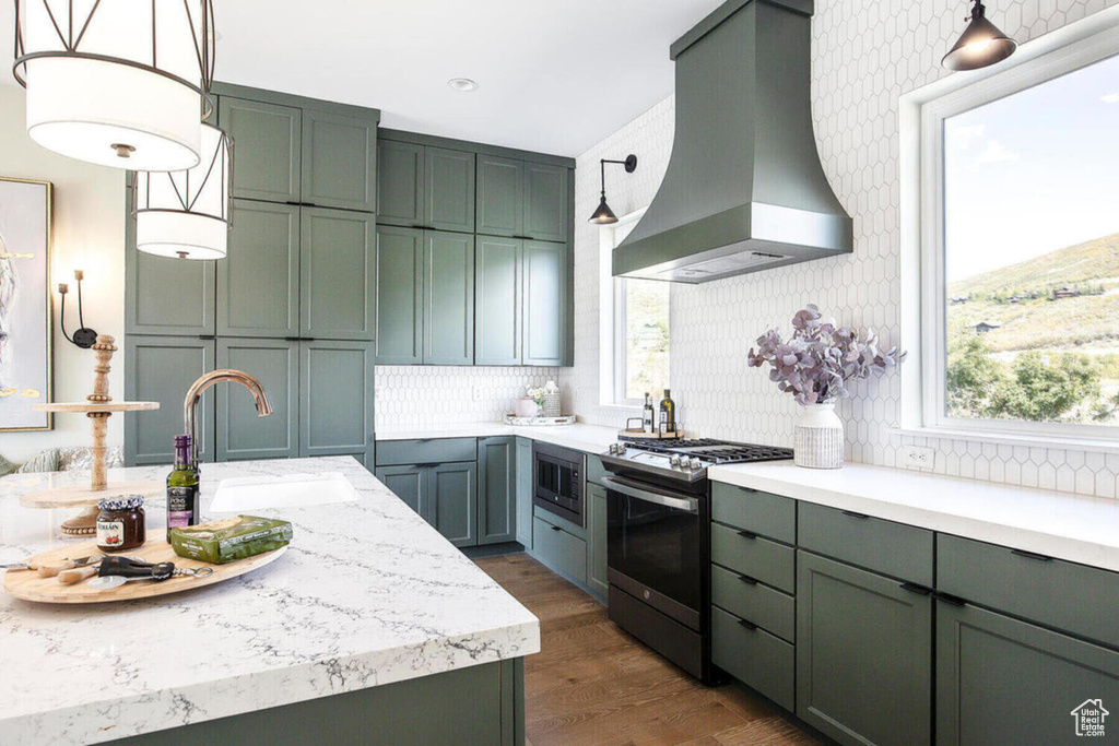 Kitchen featuring wall chimney exhaust hood, decorative light fixtures, sink, stainless steel appliances, and backsplash