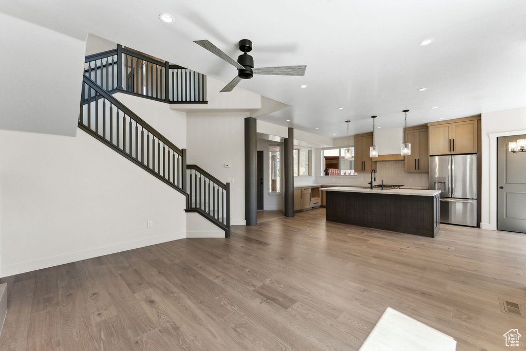 Kitchen with stainless steel fridge, sink, decorative light fixtures, a kitchen island with sink, and hardwood / wood-style flooring