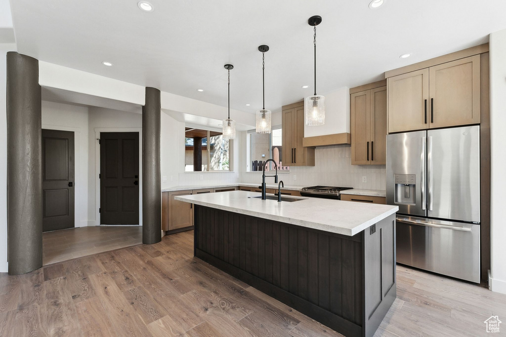 Kitchen featuring an island with sink, hanging light fixtures, sink, light hardwood / wood-style flooring, and appliances with stainless steel finishes