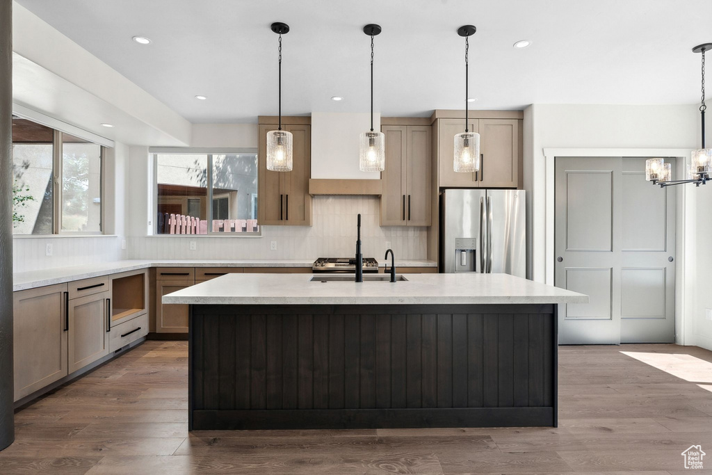 Kitchen featuring pendant lighting, sink, wood-type flooring, a kitchen island with sink, and stainless steel fridge with ice dispenser