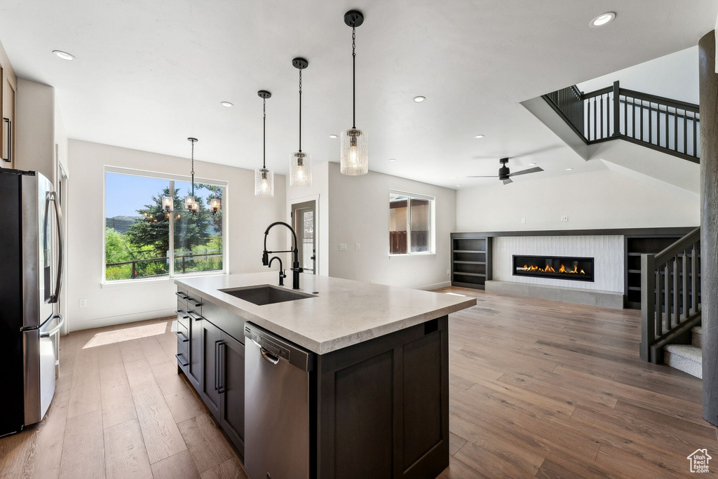 Kitchen with an island with sink, hanging light fixtures, sink, appliances with stainless steel finishes, and light wood-type flooring