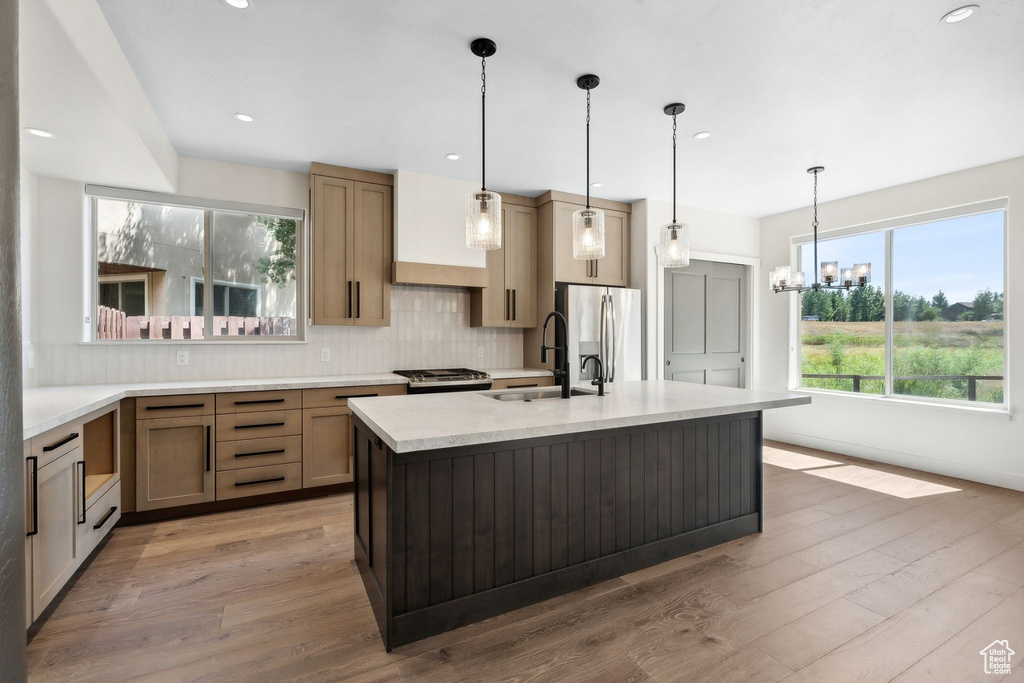 Kitchen featuring pendant lighting, a kitchen island with sink, hardwood / wood-style flooring, stainless steel appliances, and an inviting chandelier