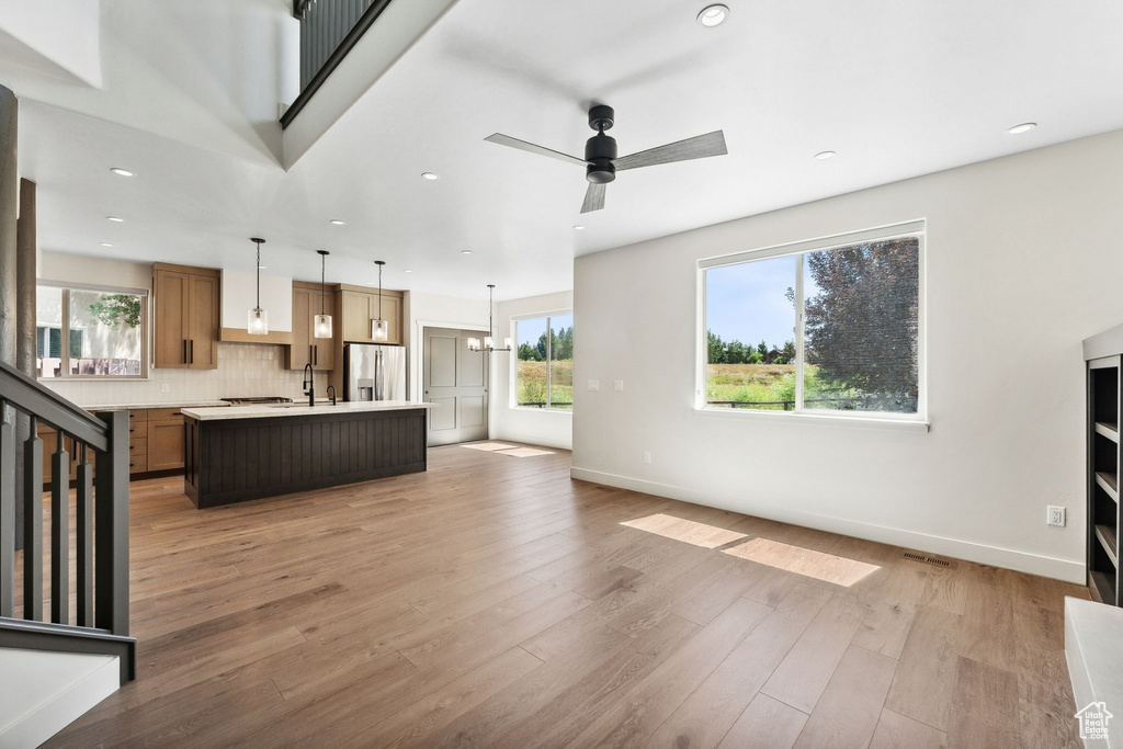 Unfurnished living room with wood-type flooring, ceiling fan with notable chandelier, and sink