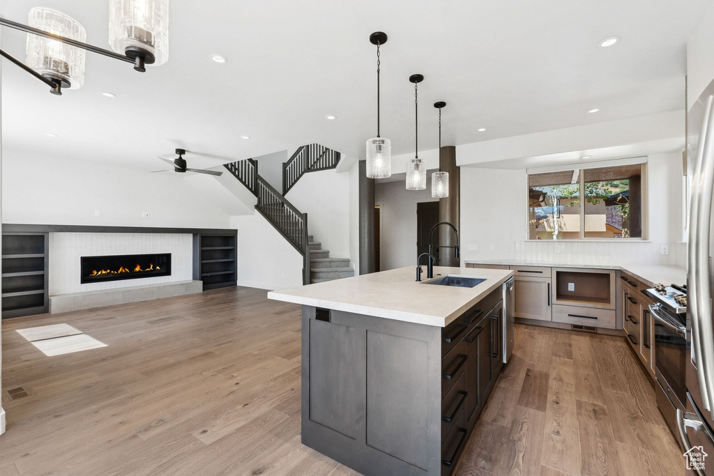 Kitchen with appliances with stainless steel finishes, a kitchen island with sink, hanging light fixtures, and light hardwood / wood-style floors