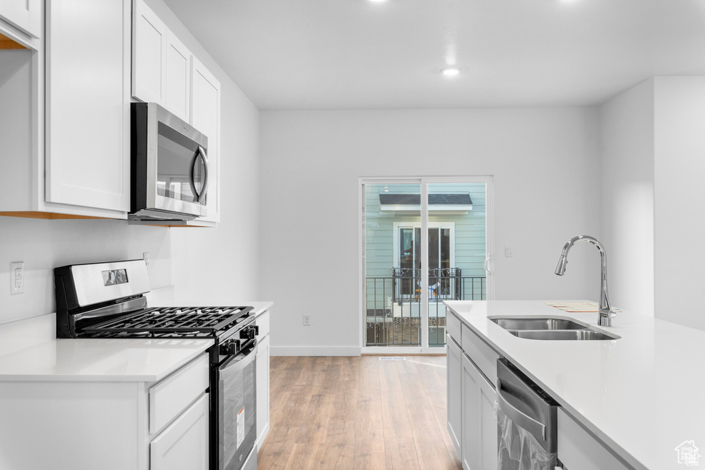 Kitchen with light hardwood / wood-style flooring, stainless steel appliances, sink, and white cabinetry