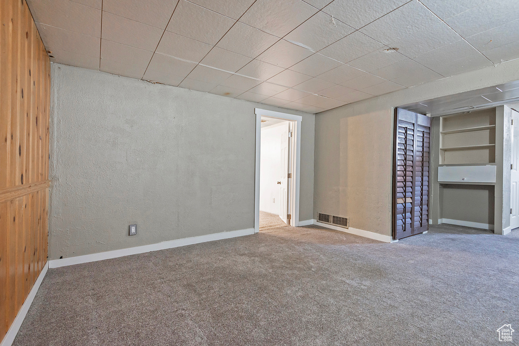 Carpeted empty room featuring wooden walls