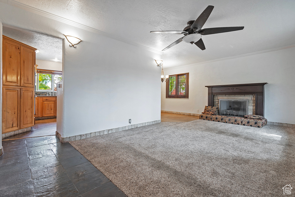 Unfurnished living room with ornamental molding, a textured ceiling, a fireplace, and dark colored carpet