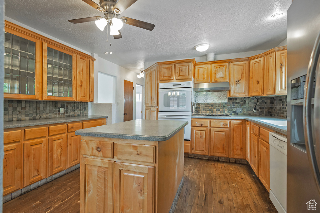 Kitchen with appliances with stainless steel finishes, backsplash, dark hardwood / wood-style flooring, and a center island