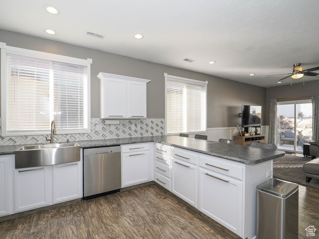 Kitchen with white cabinets, sink, kitchen peninsula, stainless steel dishwasher, and dark wood-type flooring