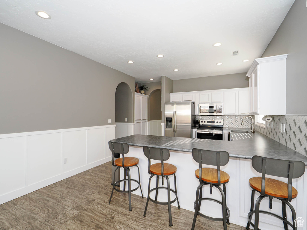 Kitchen featuring a kitchen breakfast bar, sink, stainless steel appliances, backsplash, and white cabinetry