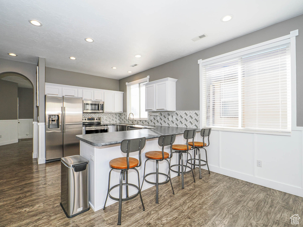 Kitchen featuring kitchen peninsula, tasteful backsplash, white cabinetry, stainless steel appliances, and dark hardwood / wood-style flooring