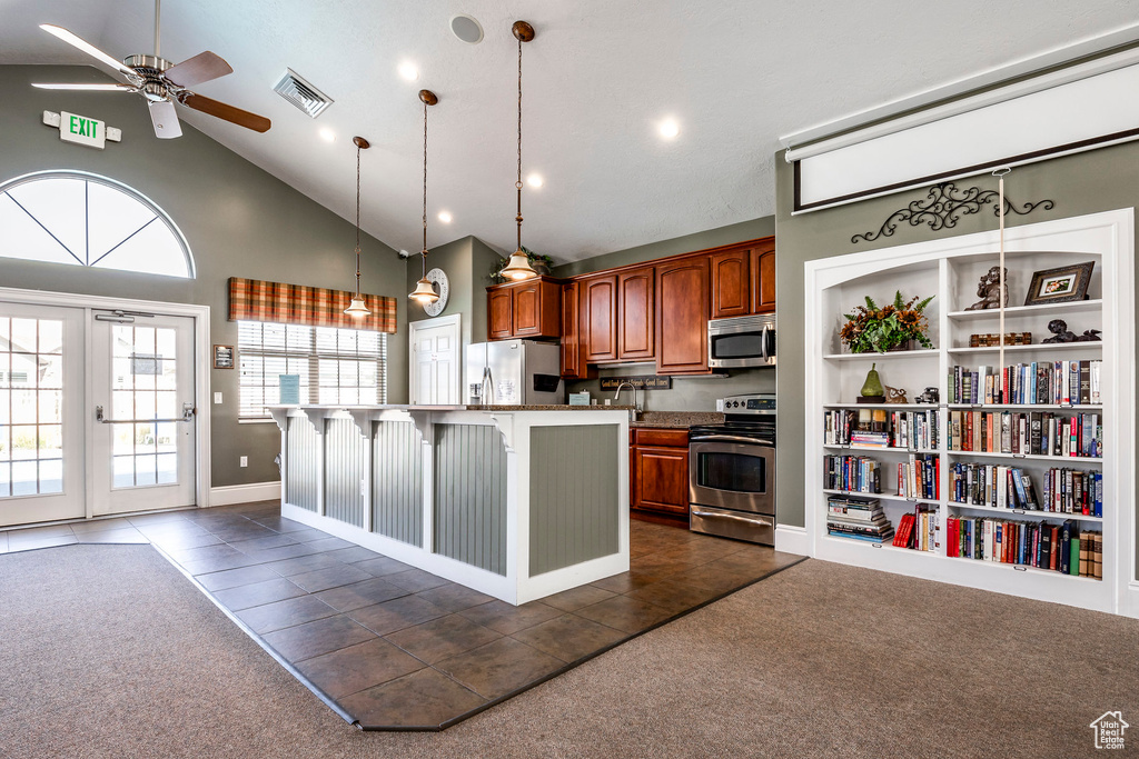 Kitchen with stainless steel appliances, dark tile patterned flooring, an island with sink, high vaulted ceiling, and a breakfast bar