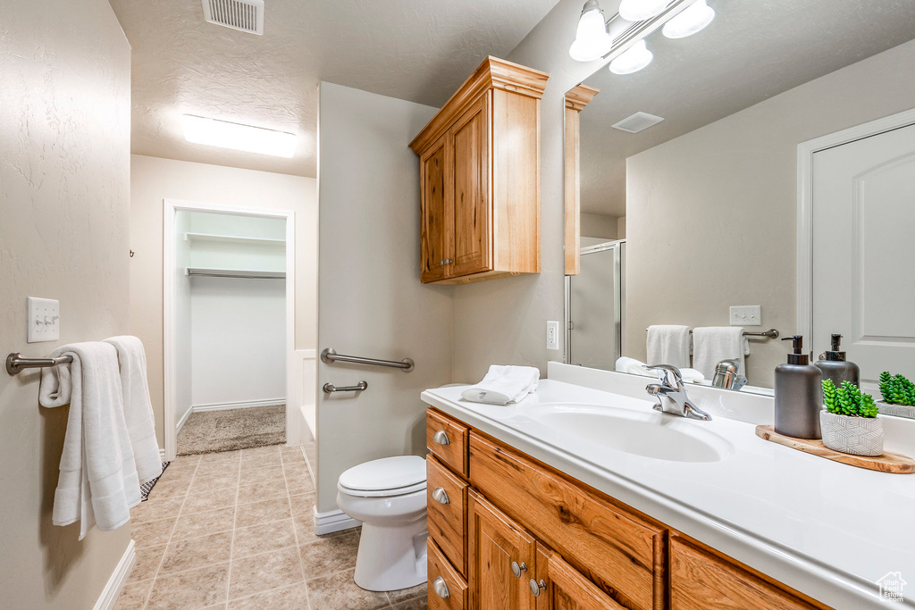 Bathroom featuring tile patterned flooring, a textured ceiling, vanity, an enclosed shower, and toilet