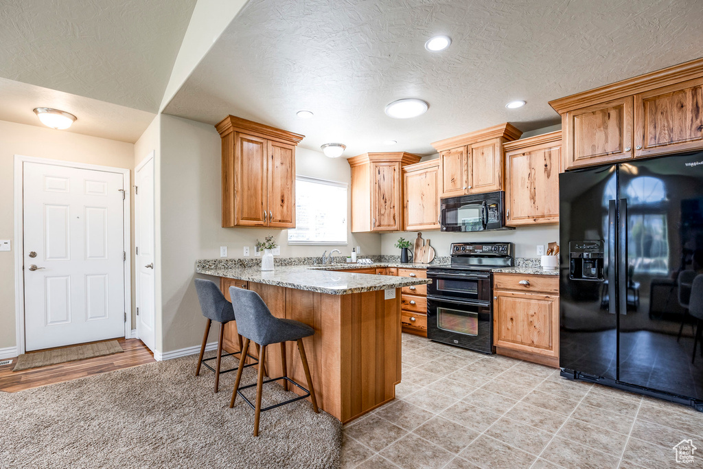 Kitchen featuring light stone counters, kitchen peninsula, black appliances, a breakfast bar area, and sink