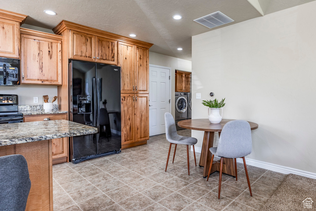 Kitchen with washing machine and clothes dryer, black appliances, a textured ceiling, and light stone countertops