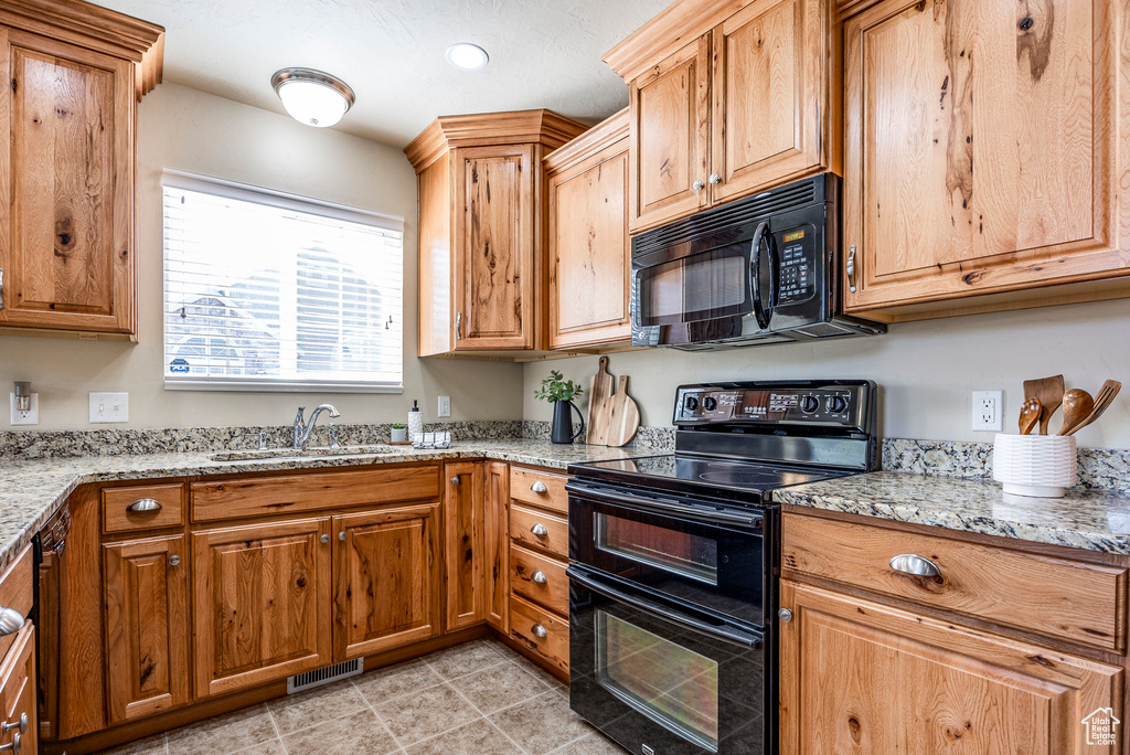 Kitchen with black appliances, sink, light stone counters, and light tile patterned floors