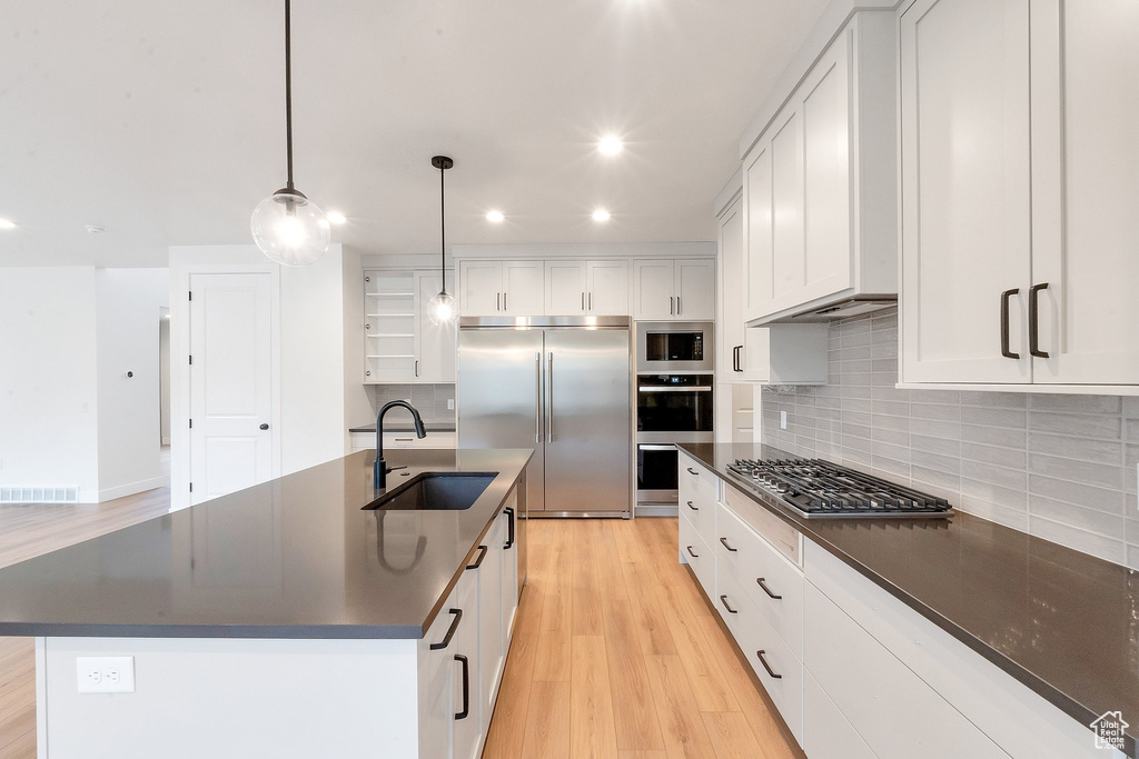 Kitchen featuring sink, hanging light fixtures, white cabinetry, built in appliances, and a kitchen island with sink