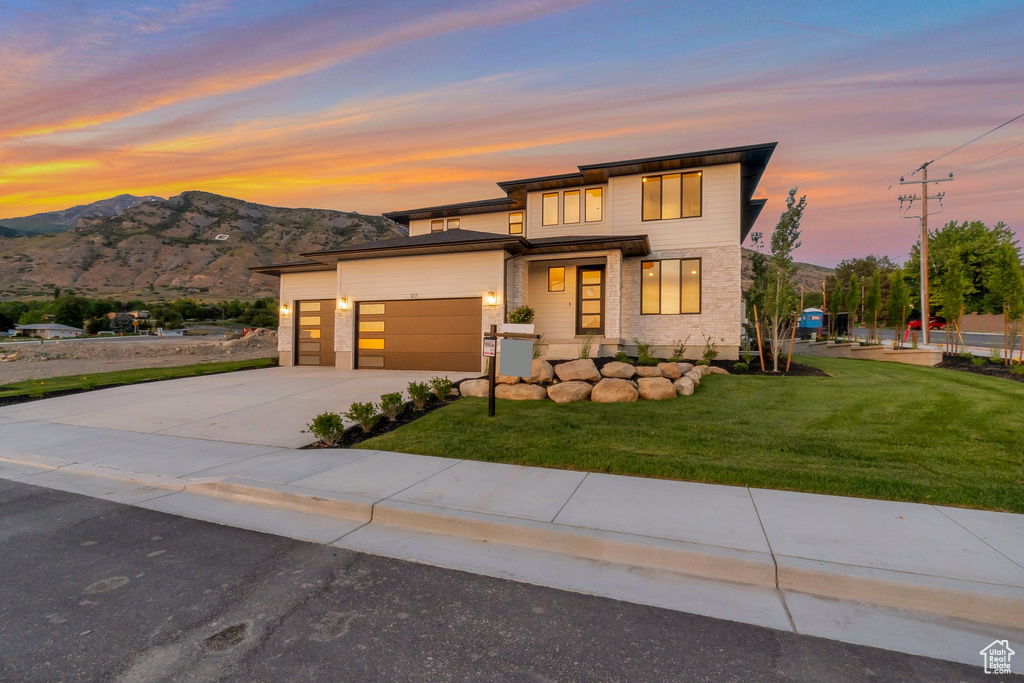 View of front of home featuring a garage, a yard, driveway, and a mountain view